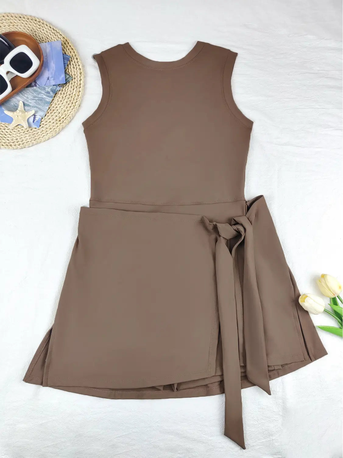a sleeveless brown skirt sport dress with a fitted bodice, flared skirt, and matching fabric belt tied into a bow at the waist, ideal as a yoga tennis skirt.