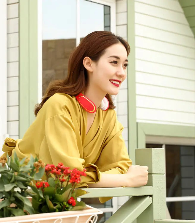 A woman wearing red and white wireless neckband headphones using an electric smart shoulder massager with heating for pain relief.
