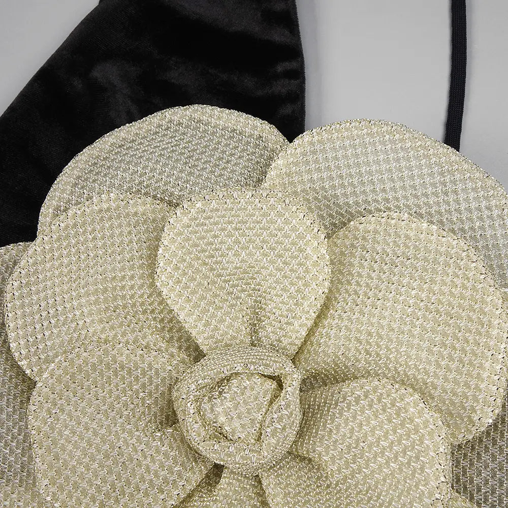 a textured cream-colored woven flower accessory with layered petals complementing a black camisole backless slim fit velvet floral gown