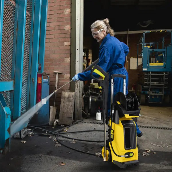 Yellow high pressure cleaning machine with hose reel featuring a yellow and black pressure cleaning machine with a long hose cleaning a blue metal gate.