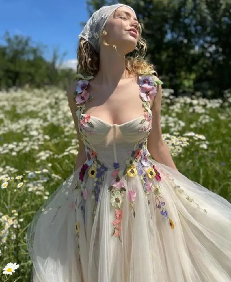 a flowing off-white light champagne tulle prom dress adorned with vibrant multi-colored floral appliqués and delicate lace detailing
