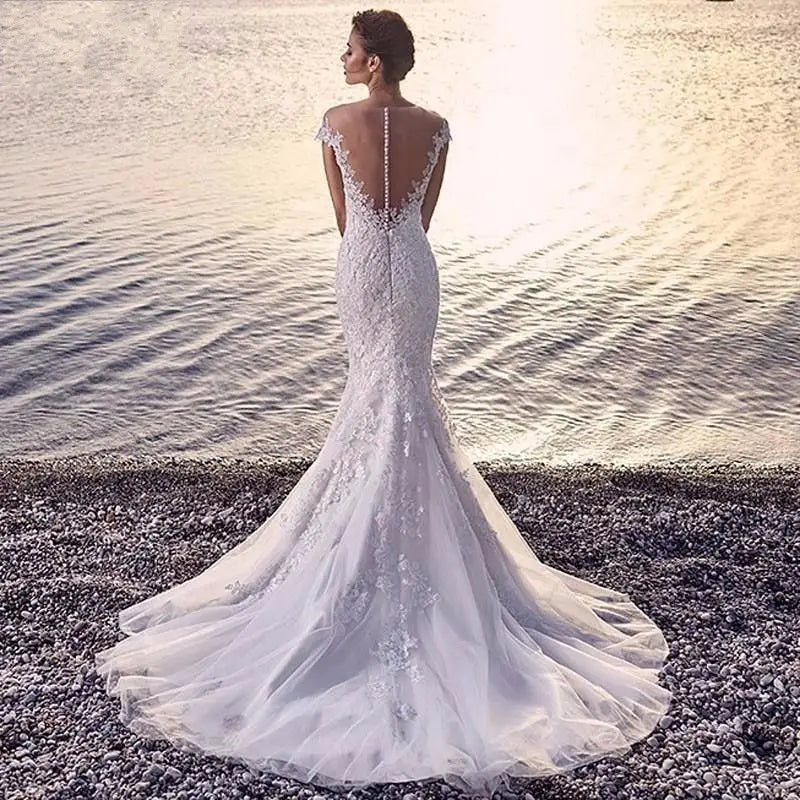 White lace princess bride mermaid wedding dress featuring an intricate back design and a flowing train with lace as the main fabric.