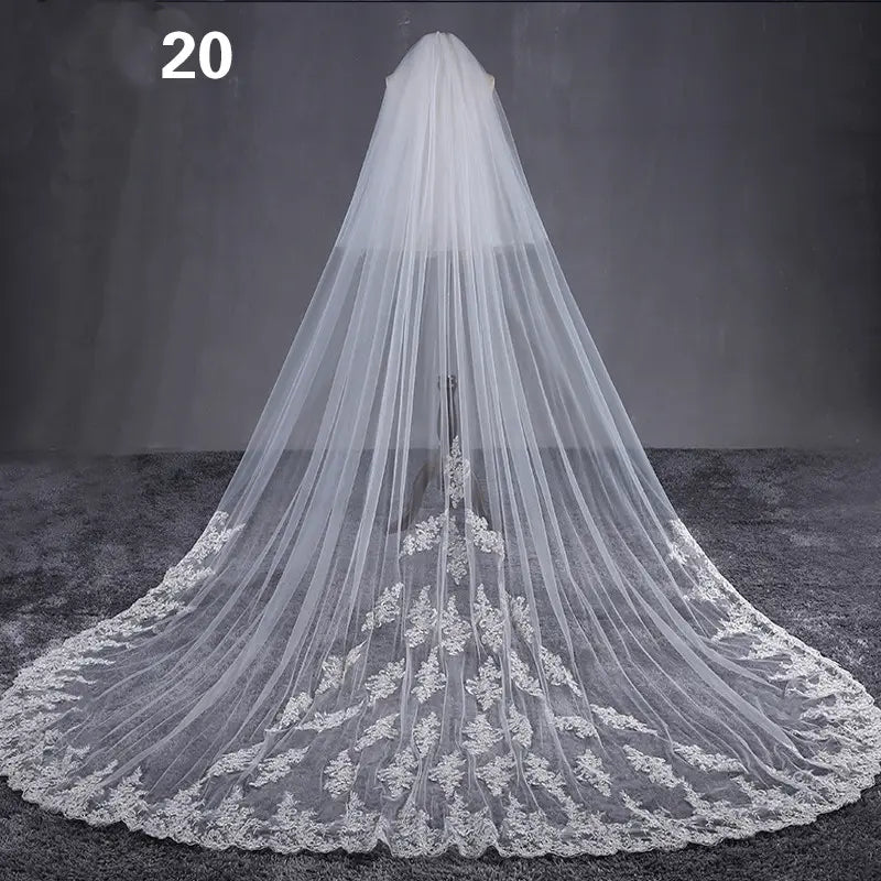 a long flowing white bridal veil made of sheer tulle with intricate lace appliqués along the hem featuring a meters wide style design