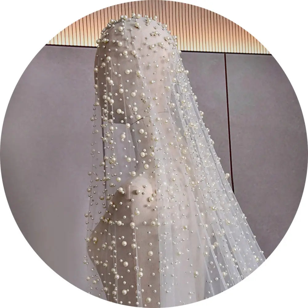 a luxury heavy industry bridal pearl veil featuring a delicate sheer white fabric adorned with numerous small evenly spaced pearls cascading down its length, paired with a tiara