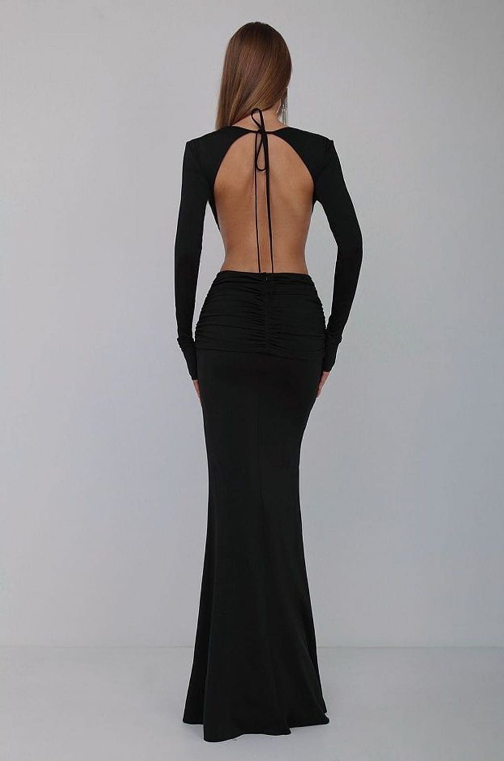 black back side view of a backless long sleeves mermaid gown with a v-neck and skirt waist tie detail