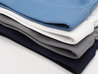 Stack of neatly folded ribbed knit pants in light blue white gray and navy paired with a white ribbed long sleeve yoga set featuring chest pad slim fit for comfortable activewear.