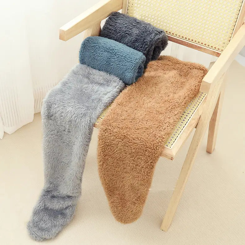 three plush fuzzy long socks in tan paw print gray and teal displayed on a wooden chair