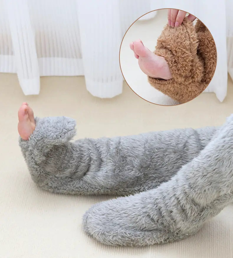 gray fluffy footie pajamas made of soft plush material with a cozy warm design paired with tan paw print fuzzy long socks for comfortable loungewear.