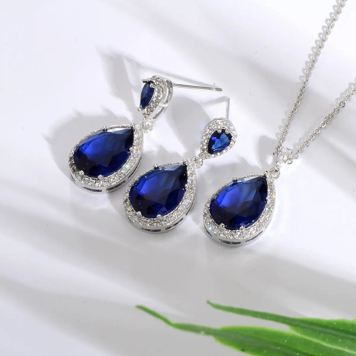 Elegant navy blue teardrop pendant necklace and matching earrings set featuring bright big zircon sparkling clear gemstones encased in silver-toned metal.