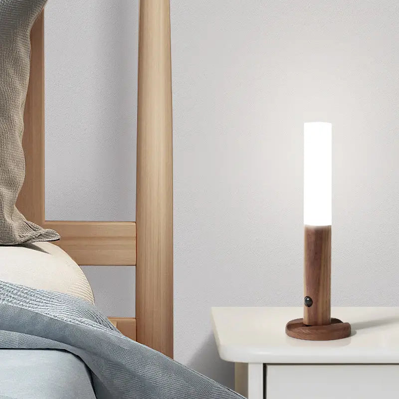 A sleek cylindrical wooden led desk lamp sconce with a frosted glass warm white illuminated top and a natural wood base.