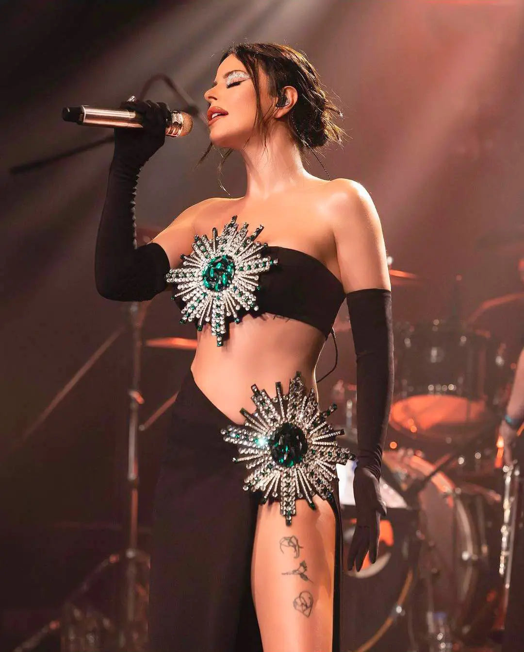 black strapless bodice and matching high slit skirt bandage suit adorned with two large radiant emerald green crystal sunburst embellishments featuring shiny rhinestone tube detailing