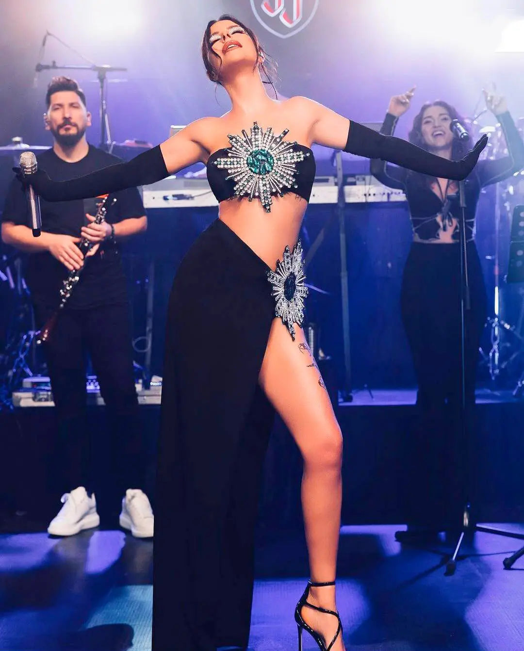 black strapless bodice with radiant starburst design featuring sparkling crystals and a central emerald green stone on a shiny rhinestone tube high slit skirt bandage suit