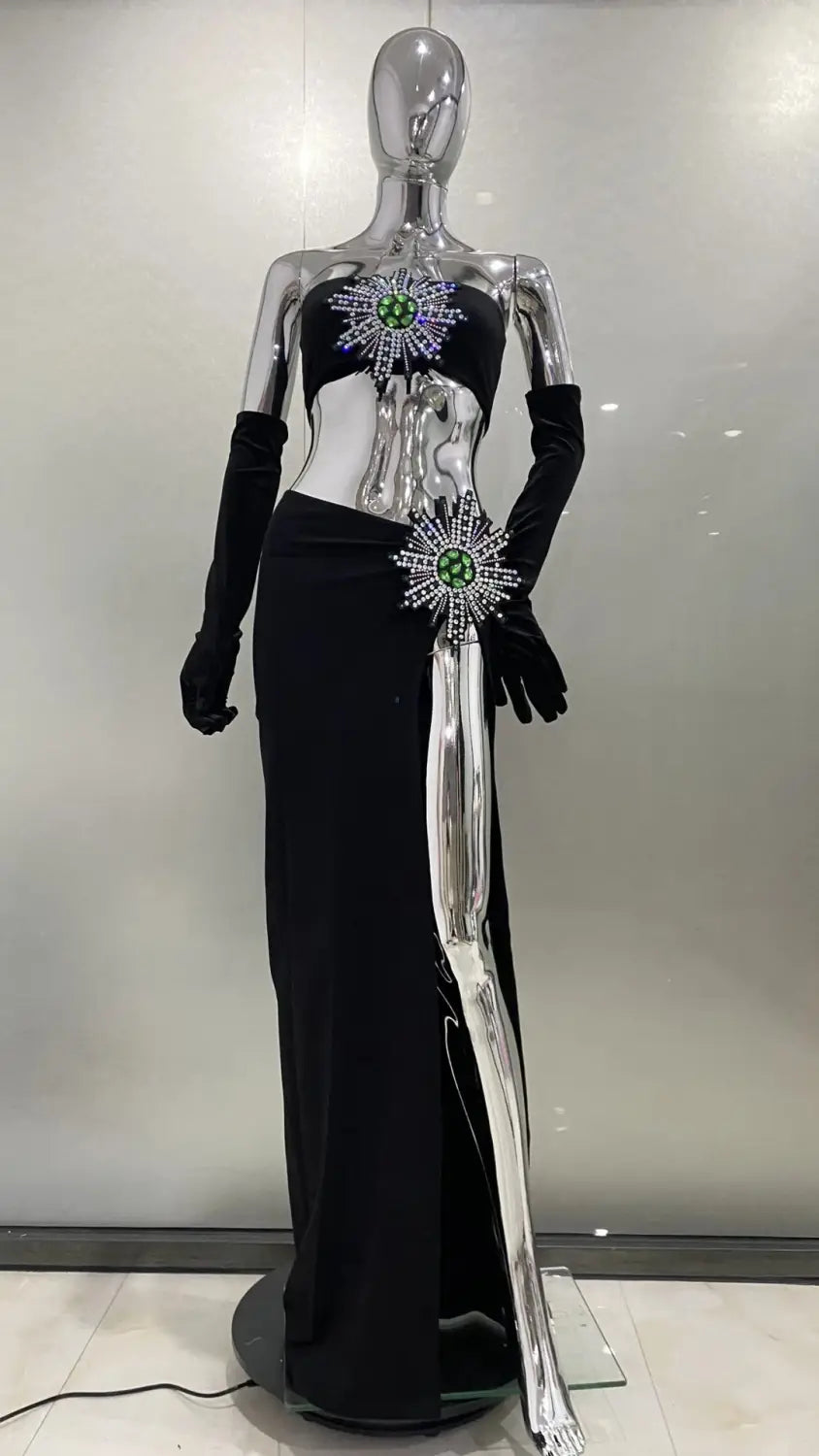 Black satin strapless gown featuring a shiny rhinestone tube high slit skirt bandage design with silver metallic side slit and embellished green gemstone starburst accents at the bust and waist.