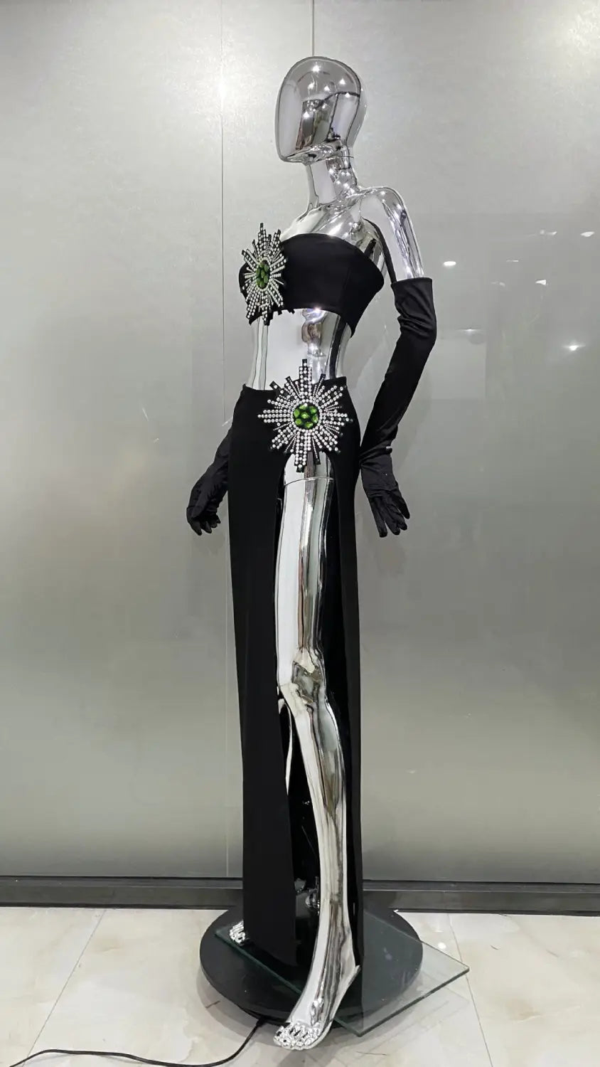 Black and silver metallic shiny rhinestone tube high slit skirt bandage suit featuring intricate starburst embellishments with green gemstones.