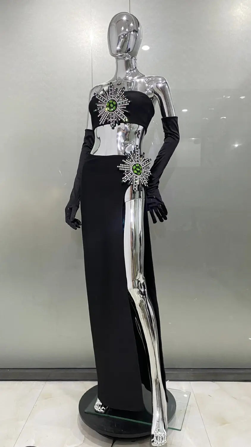 black satin strapless shiny rhinestone tube gown featuring a high slit skirt bandage design with silver metallic side slit and green gemstone starburst embellishments.