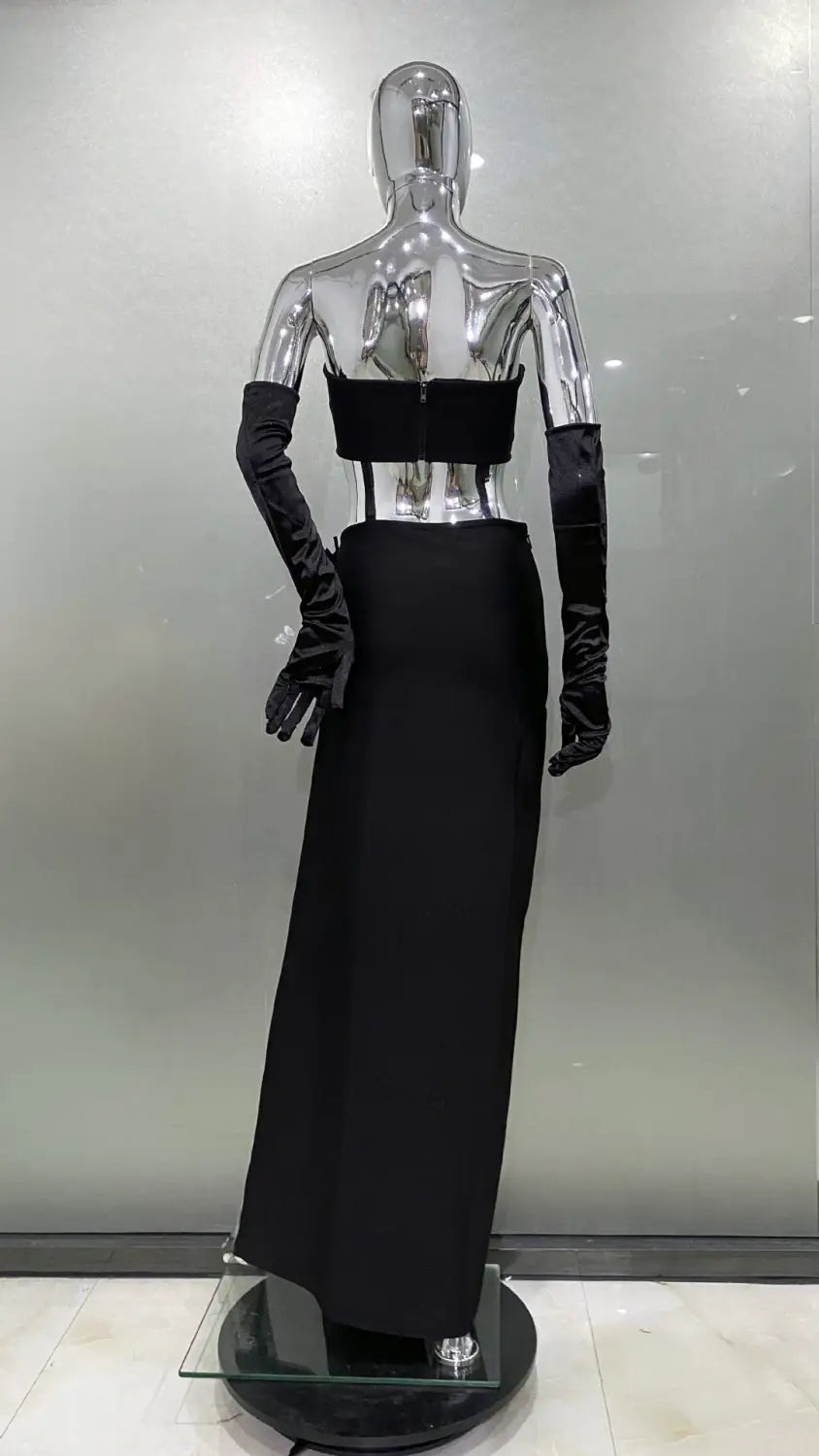 Elegant black satin strapless gown with a structured bodice and high slit skirt displayed on a reflective silver mannequin as a shiny rhinestone tube slit skirt bandage suit.