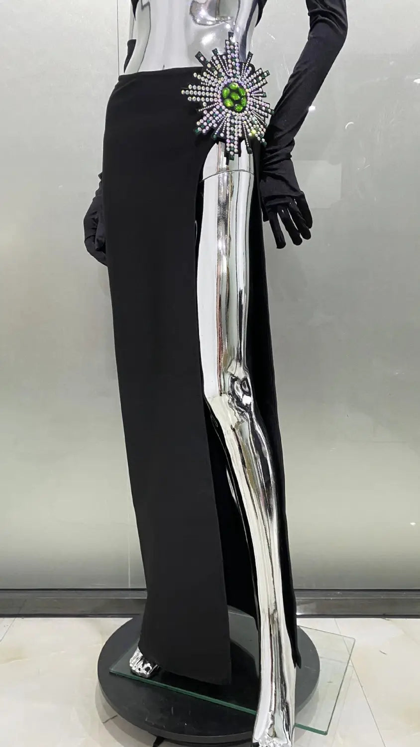 black high-waisted shiny rhinestone tube slit skirt bandage trousers with a reflective silver high slit and a large sparkling green gemstone brooch at the waist