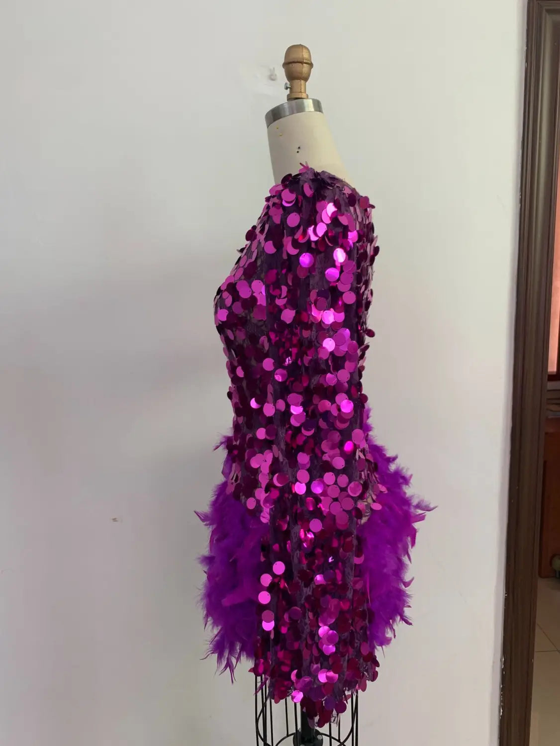 a dazzling purple sequined feather sleeve short dress with a fuchsia sequined feather skirt and a feathered hemline displayed on a mannequin
