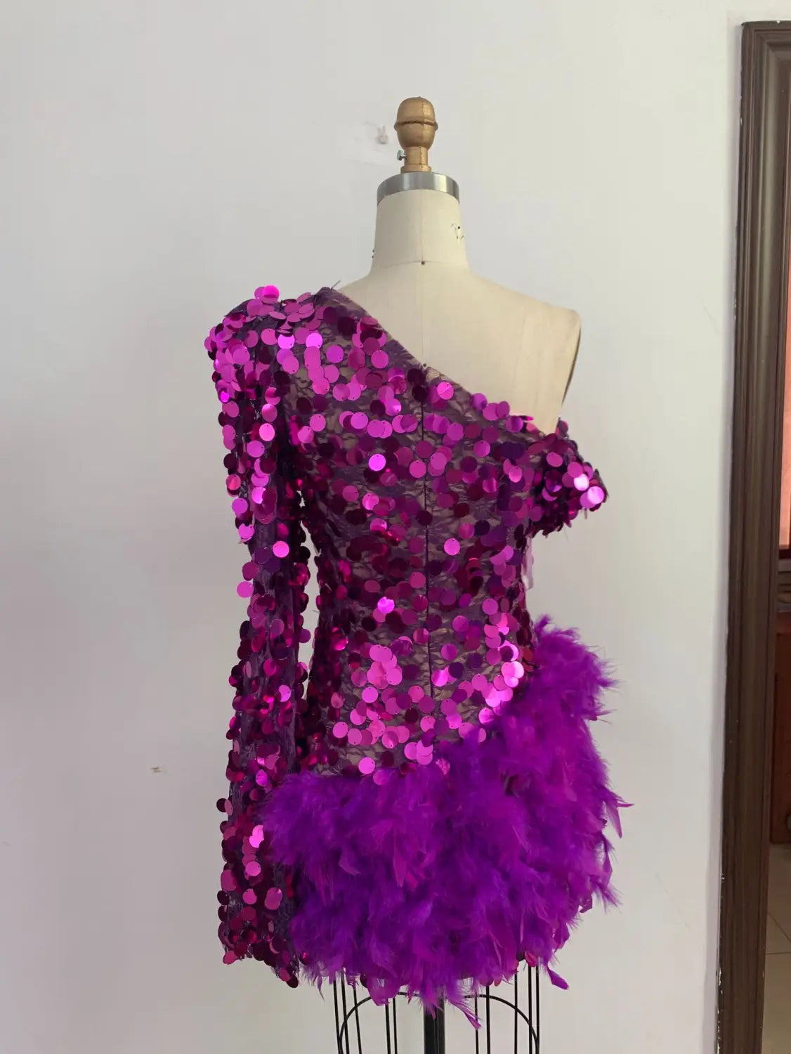 A vibrant magenta purple sequined feather sleeve short dress featuring a one-shoulder design and a sequined feather skirt hemline.
