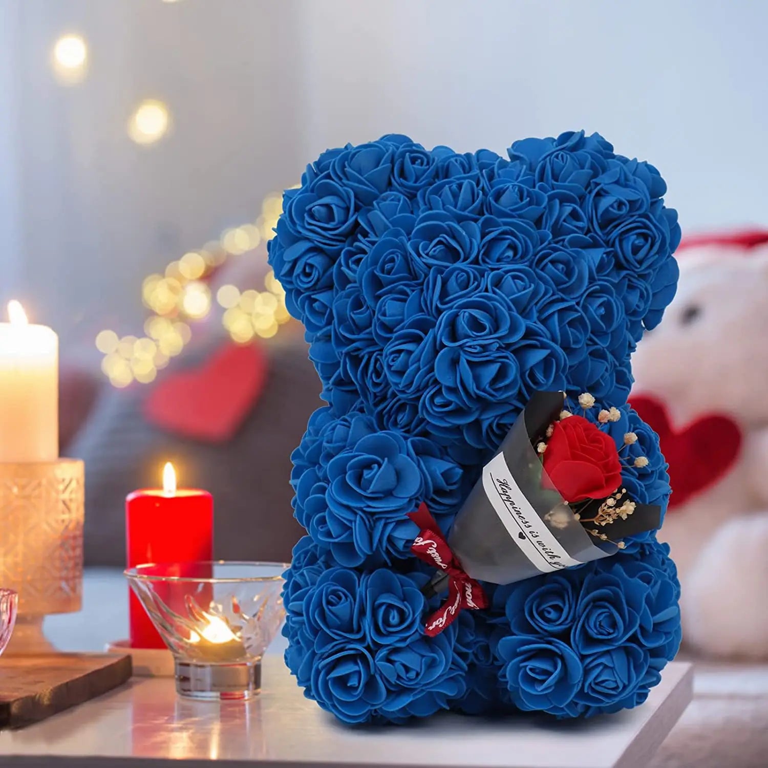 a plush blue rose bear made of artificial eternal flowers holding a small bouquet of red and white flowers in its paw presented in a red rose bear eternal flower gift box