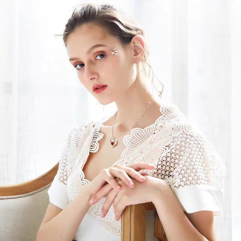 white lace butterfly-shaped shoulder cape with delicate crochet detailing and short flutter sleeves paired with a gold heart red sapphire pendant necklace featuring a vibrant red sapphire gemstone