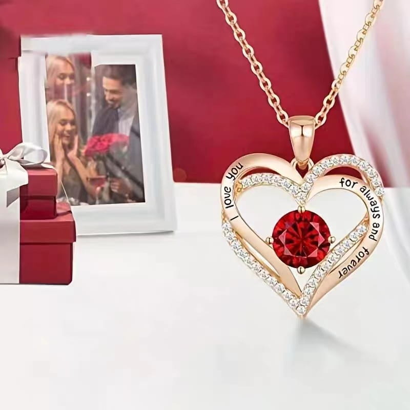 A rose gold heart-shaped sapphire pendant necklace featuring a central red sapphire gemstone surrounded by diamonds and engraved with the phrase i love you for always and forever.