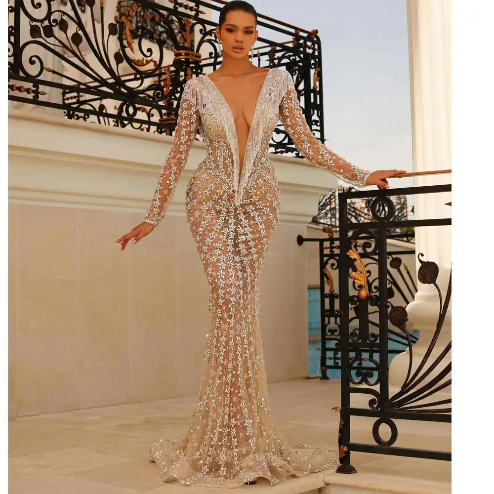 A shimmering champagne-colored backless tight fishtail gown featuring intricate silver beading lace detailing long sleeves and a plunging v-neckline.