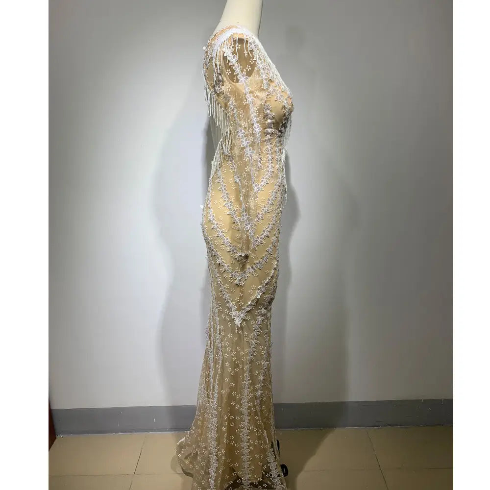 A shimmering champagne-colored backless tight fishtail gown featuring intricate white lace, delicate beading, and a sheer overlay with flowing fringe along the sides.
