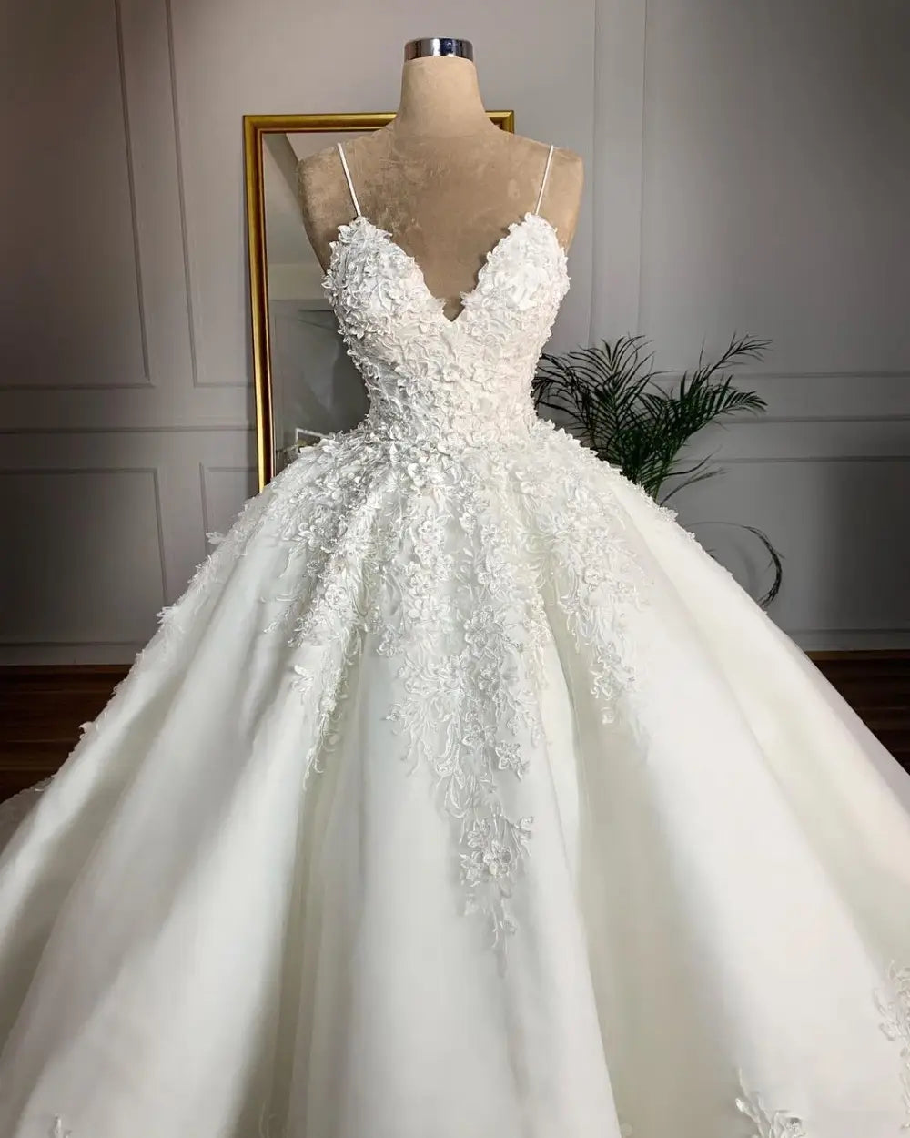 A white lace wedding dress romantic aura featuring a deep v-neck, fitted bodice, and voluminous skirt adorned with intricate floral appliqués along the front.