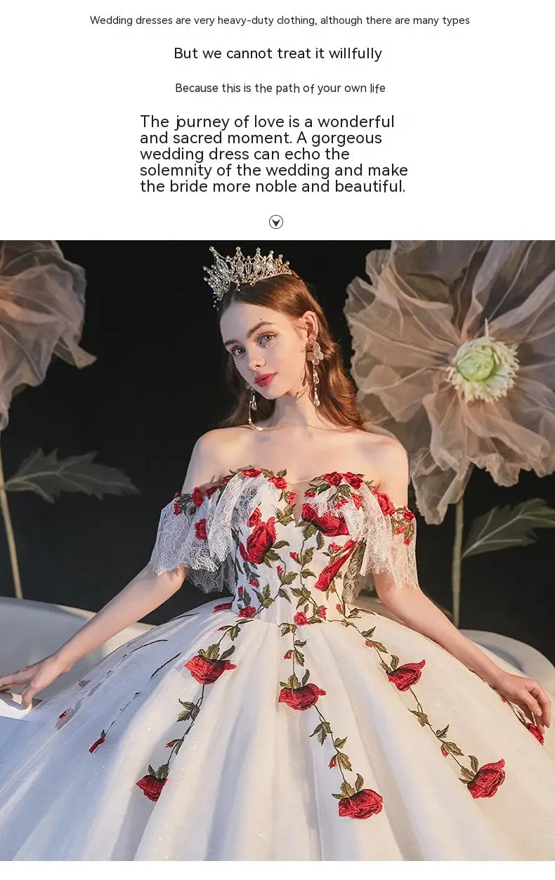 A white off-the-shoulder wedding dress featuring vibrant red rose embroidery and delicate lace detailing designed as a temperament bride bra with bride bra trailing accents.