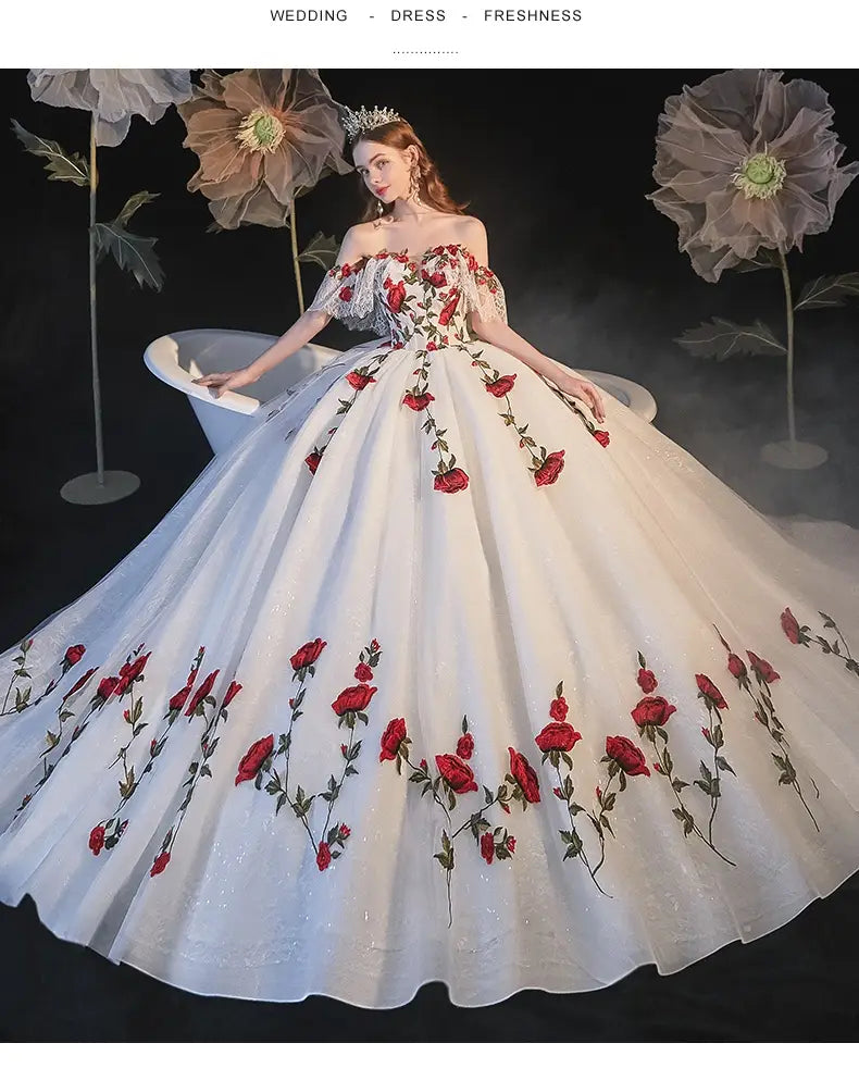 A white off-the-shoulder wedding dress with vibrant red rose embroidery and delicate silver beading featuring a voluminous skirt perfect for a temperament bride bra or bride bra trailing style.