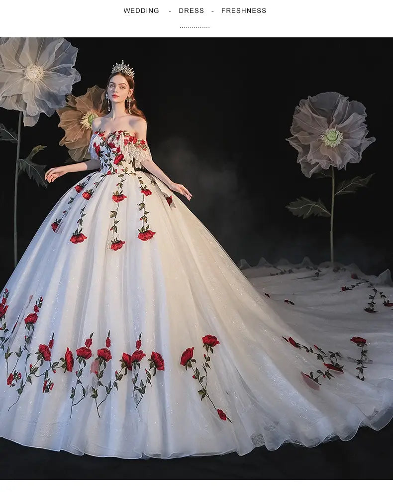 A flowing white wedding dress featuring vibrant red rose embroidery and delicate floral embellishments designed as a temperament bride bra with bride bra trailing detailing.