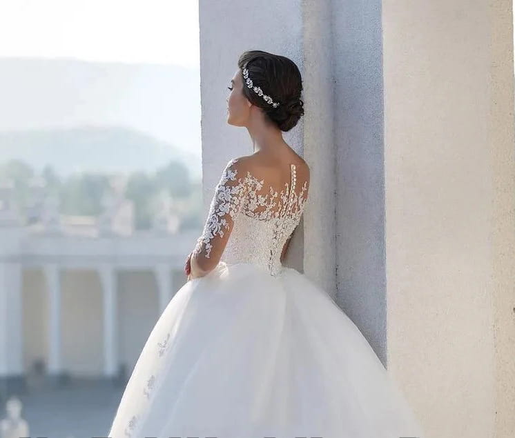 a white bridal mesh long sleeve wedding dress featuring intricate lace detailing on the shoulders and sleeves with a fitted bodice and voluminous skirt