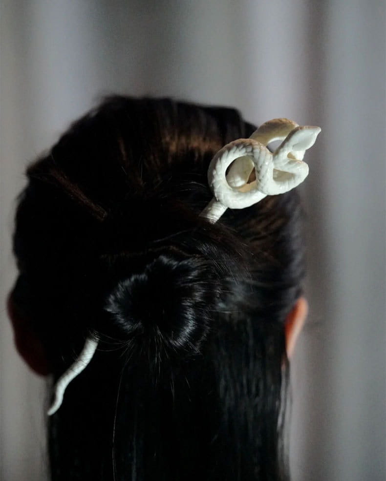a delicate white ceramic retro style hairpin shaped like an intricately coiled snake with a smooth, glossy finish