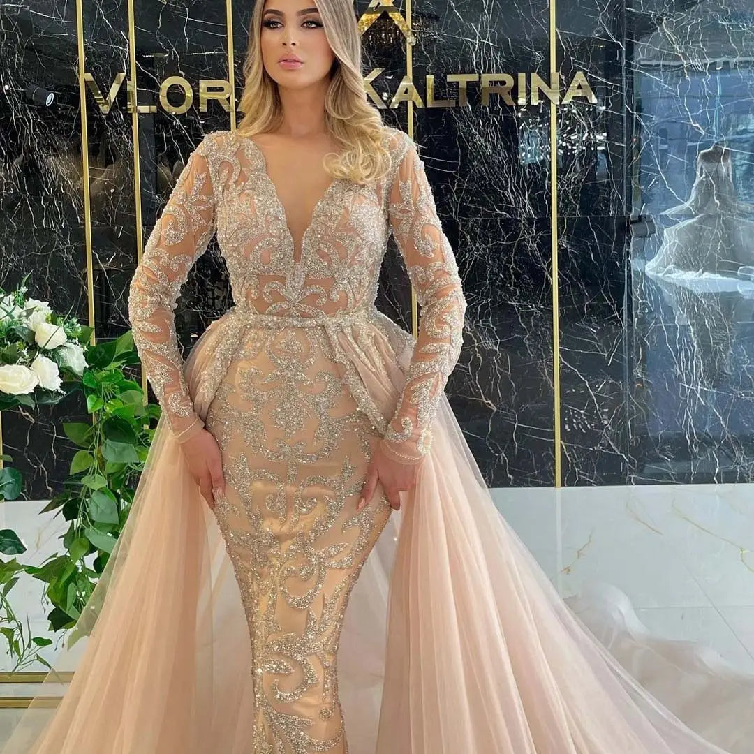 A shimmering champagne-colored blush pink beaded french style simple wedding dress features intricate gold beading, long sheer sleeves, and a flowing tulle train.