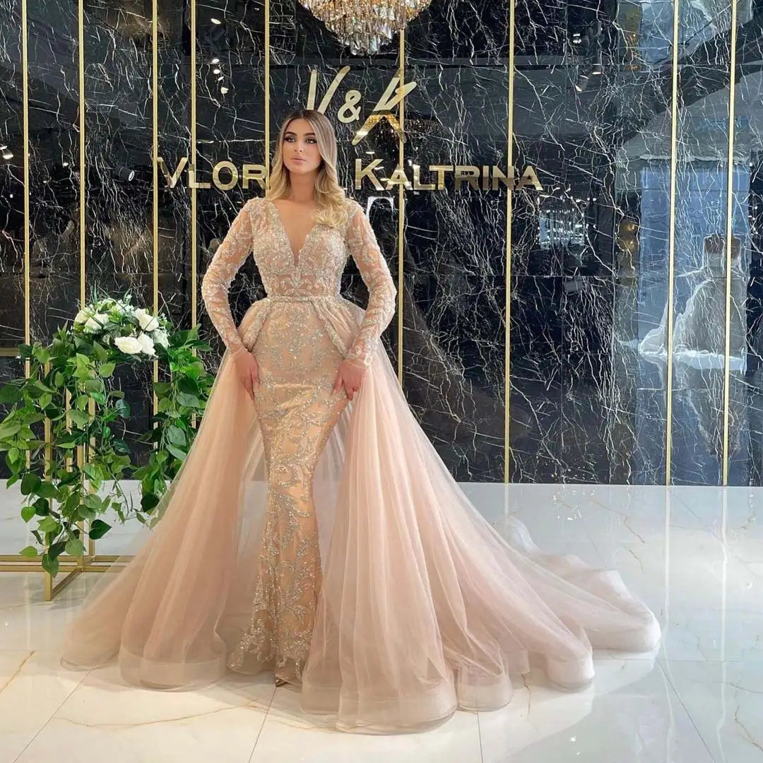 a blush pink mermaid-style wedding dress with long sleeves, intricate gold beading, a fitted bodice, and a voluminous tulle train, embodying french style simple elegance.