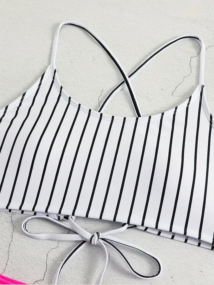 White bikini top with black vertical stripes and thin straps crossing at the back featuring a tied bow detail on the side in a pink striped bikini split swimsuit for women.