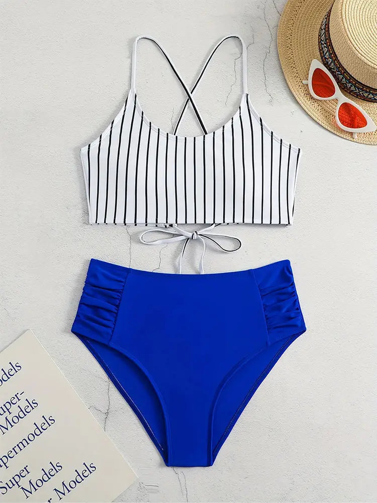 A stylish bikini split swimsuit featuring a white top with black vertical stripes and crisscross straps paired with high waisted royal blue bottoms in a pink striped bikini split design.