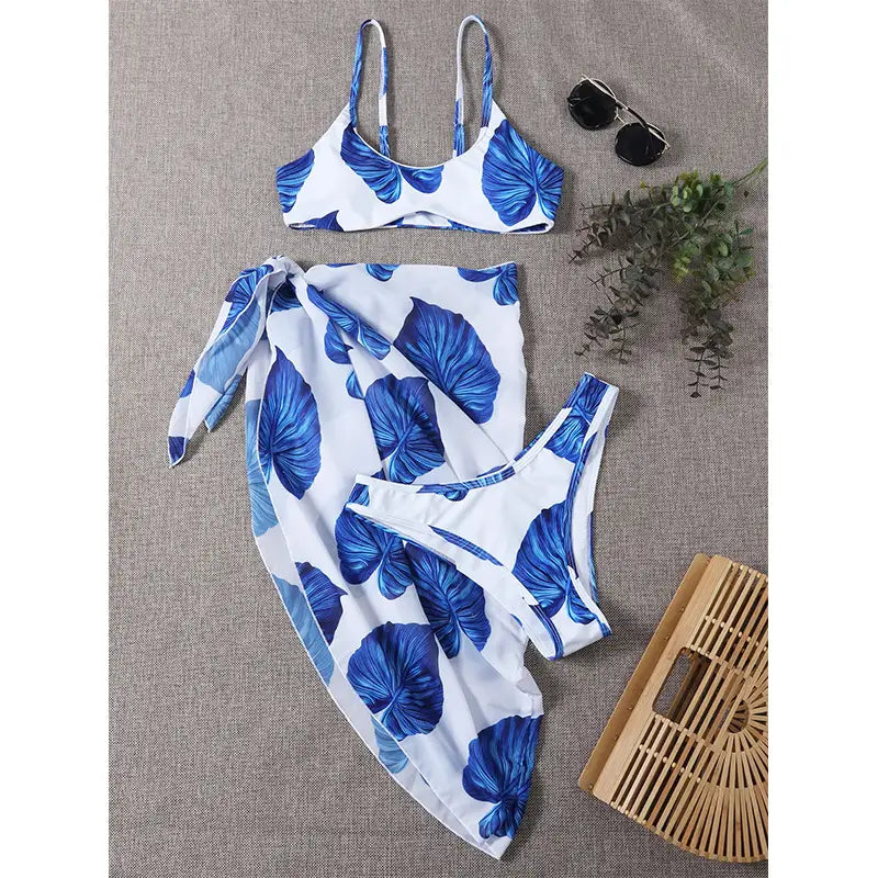 blue and white leaf-patterned bikini printed three-piece set swimsuit featuring a two-piece swimsuit with a matching wrap skirt for tropical beachwear.