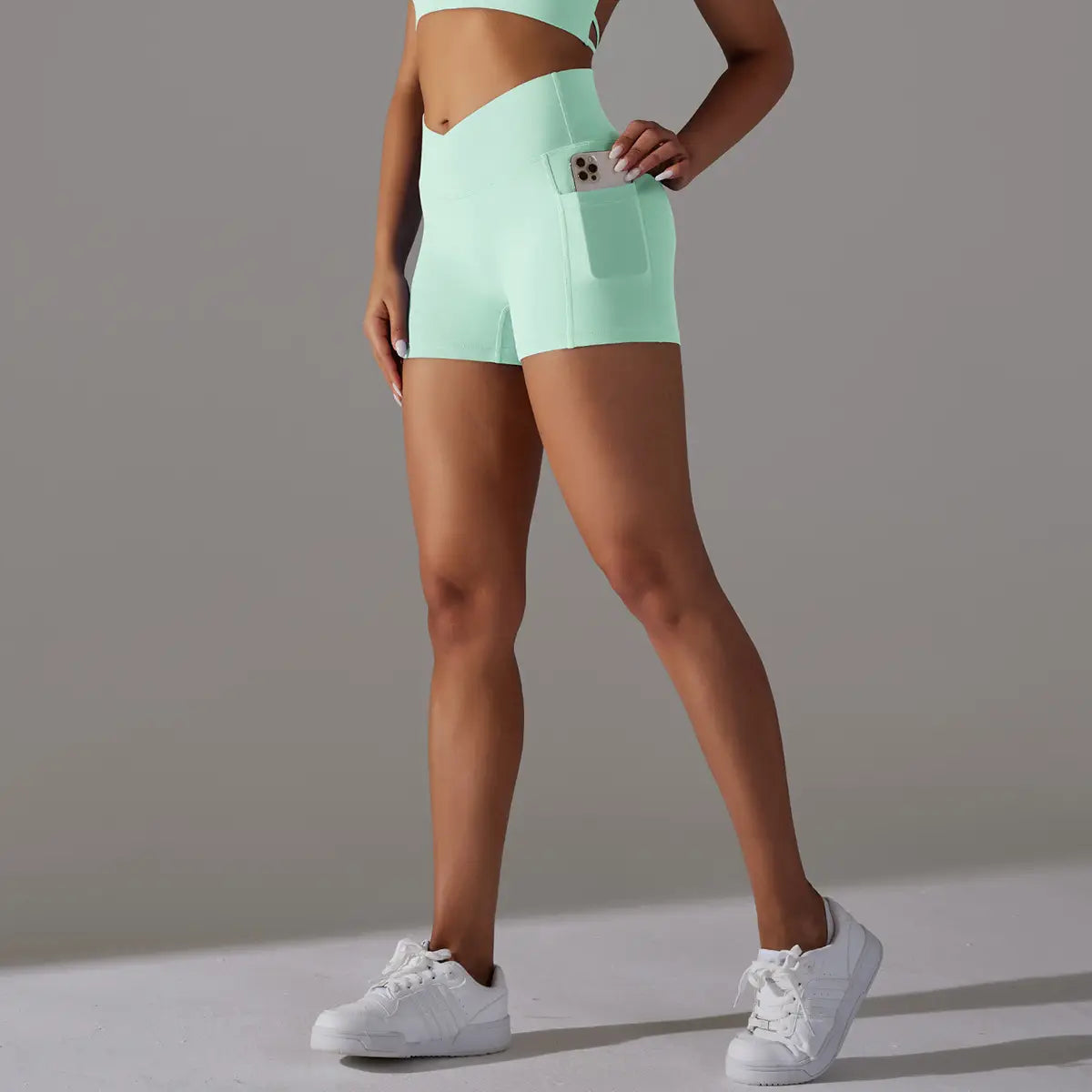 Mint green high-waisted athletic shorts with a phone pocket design held by a smartphone side pocket ideal for design fitness sports.