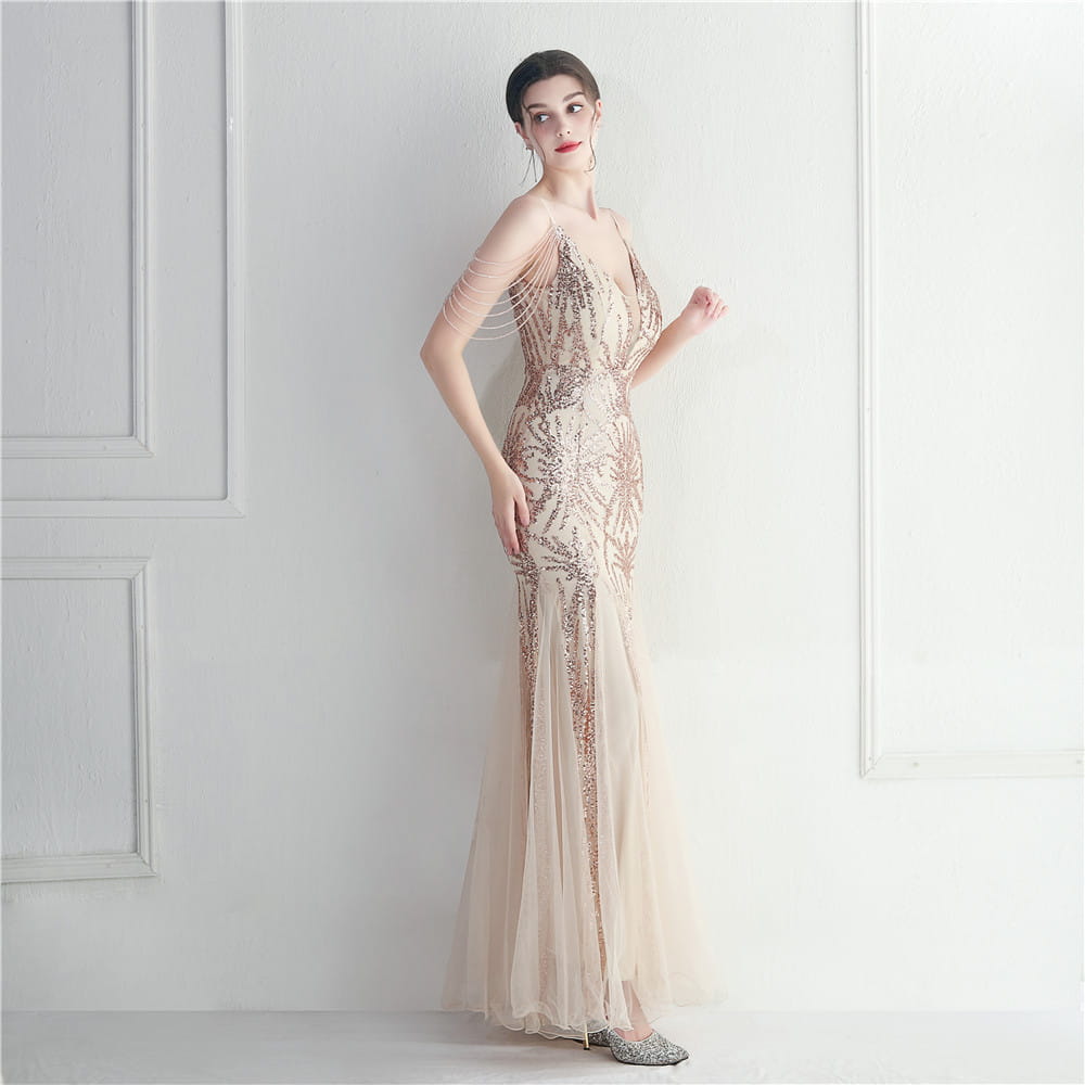 A champagne-colored mermaid gown with intricate gold sequin embroidery and sheer tulle overlay designed as a mesh beaded bridal wedding dinner gown.