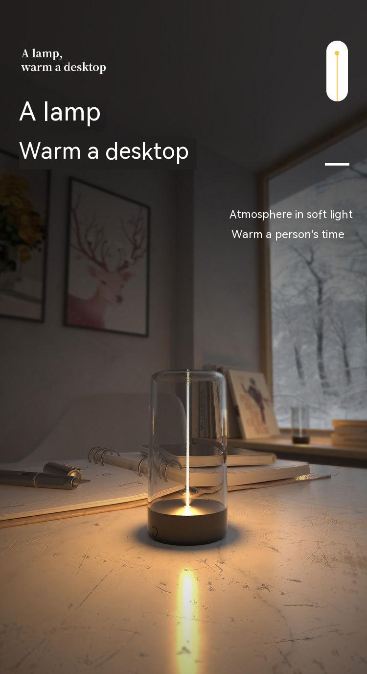 A sleek minimalist rechargeable portable night light led camping light with a clear glass cylinder and dark metallic base emitting warm light.