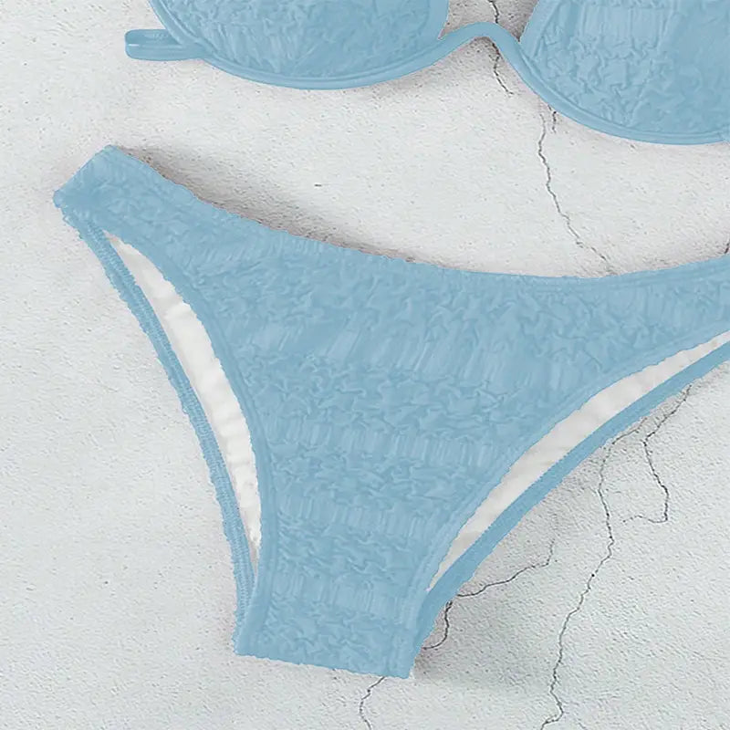light blue lace bikini bottom with white inner lining shown as part of a black lace two piece bikini split swimsuit