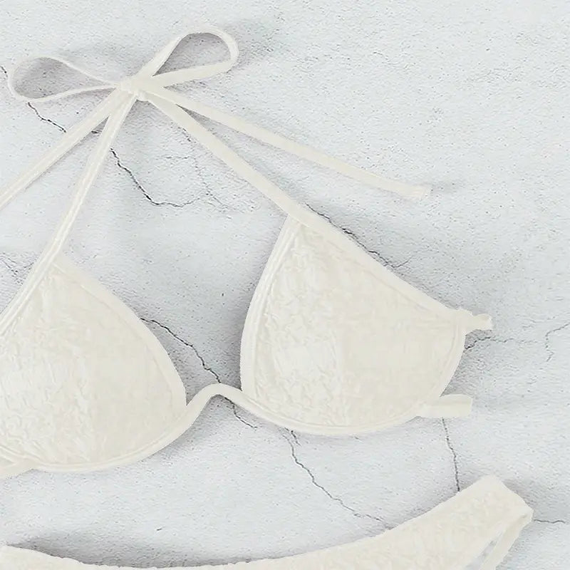 Cream-colored lace triangle bikini top with thin tie-back straps as part of a black lace two piece bikini split swimsuit.