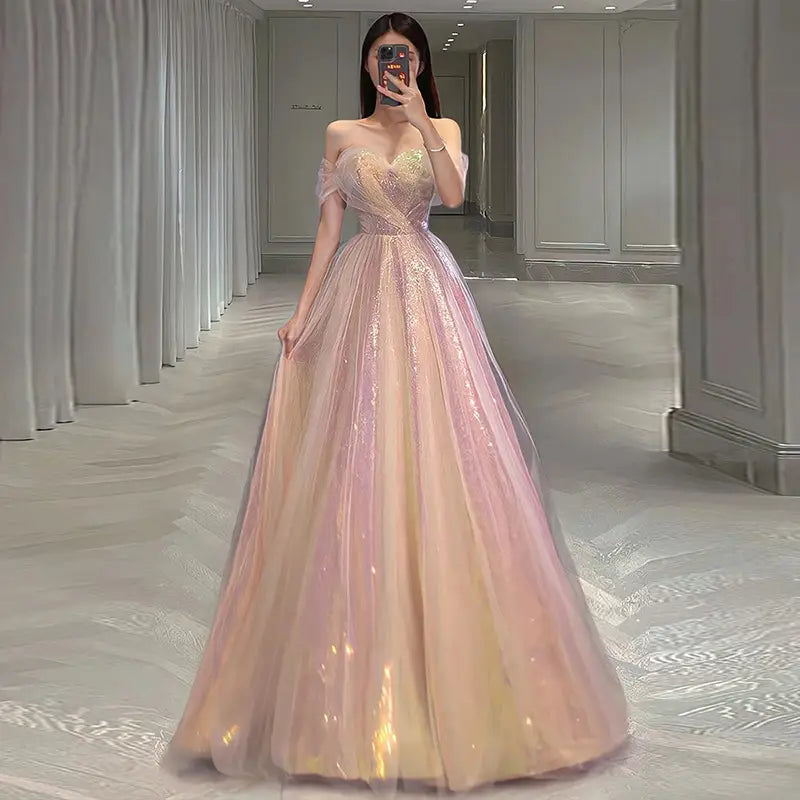 A shimmering blush and gold gradient mesh slimming annual party banquet mermaid dress with a fitted sequined bodice, off-the-shoulder sleeves, and a flowing tulle skirt.