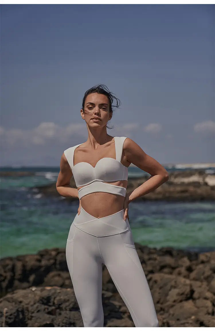 White two-piece athletic set featuring a cut-out design and seamless fabric, complementing beige yoga pants and a sport coat in deep black color for fitness activities.