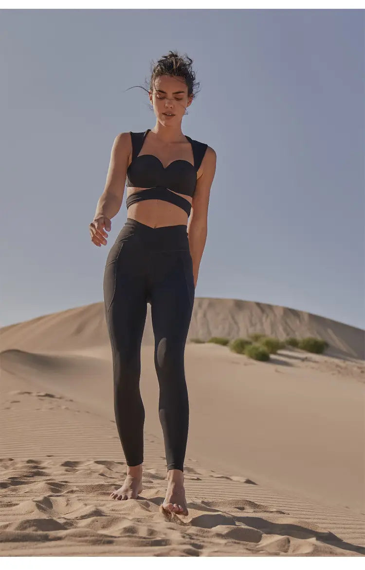 black athletic crop top with sweetheart neckline and crisscross strap design in deep black color paired with beige yoga pants and sport coat fitness set