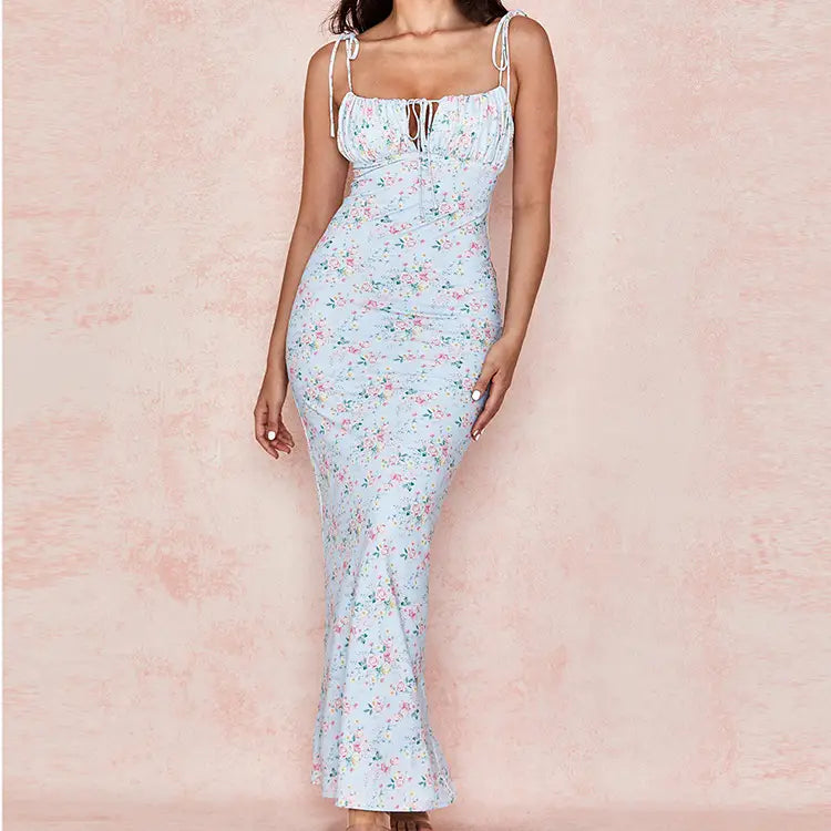 A light blue summer floral print midi dress for women featuring delicate pink and green blossoms with thin white spaghetti straps and a front tie square neckline.