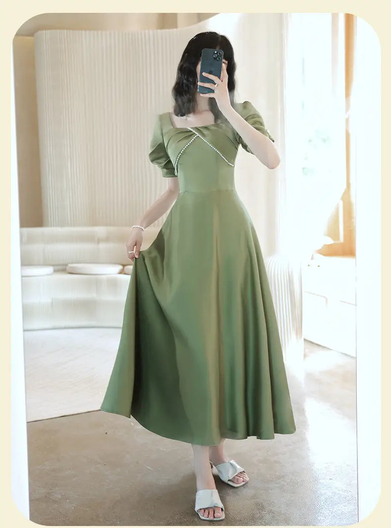 A soft avocado green sisters group midi dress made of satin with puffed short sleeves and a square neckline accented by delicate pearl-like beads.