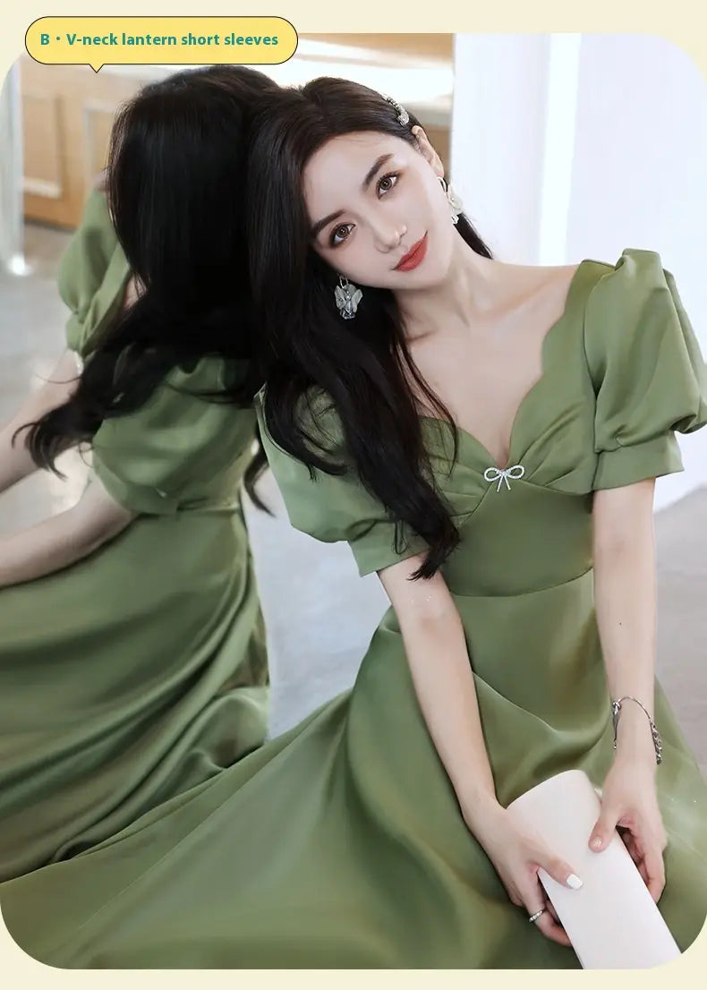 A soft avocado green sisters group satin midi dress featuring a v-neckline, lantern sleeves, and a delicate white bow at the neckline.